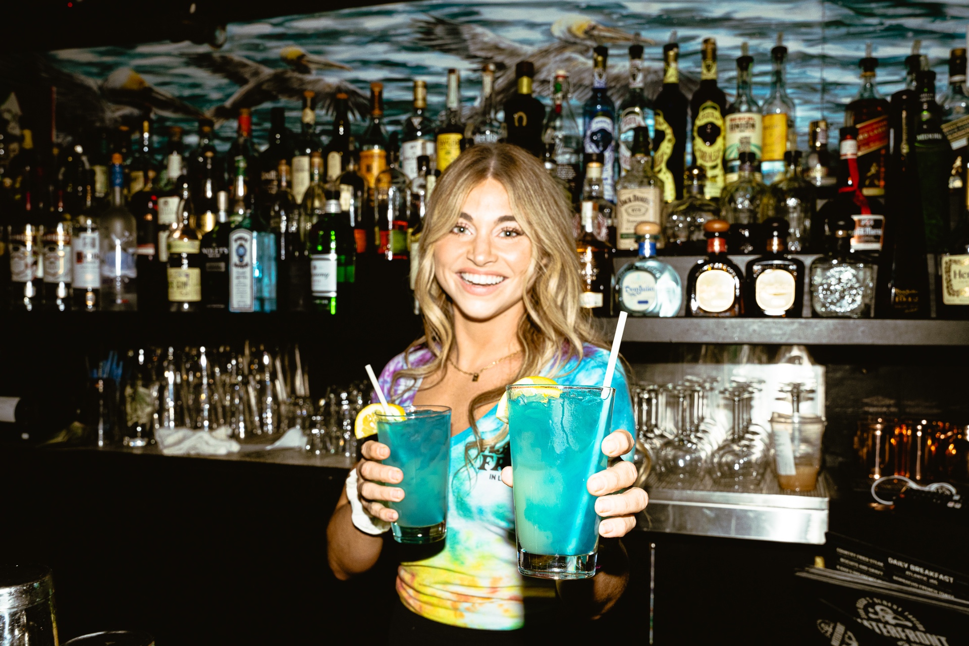 Bartender holding up two bright blue cocktails behind the Waterfront bar
