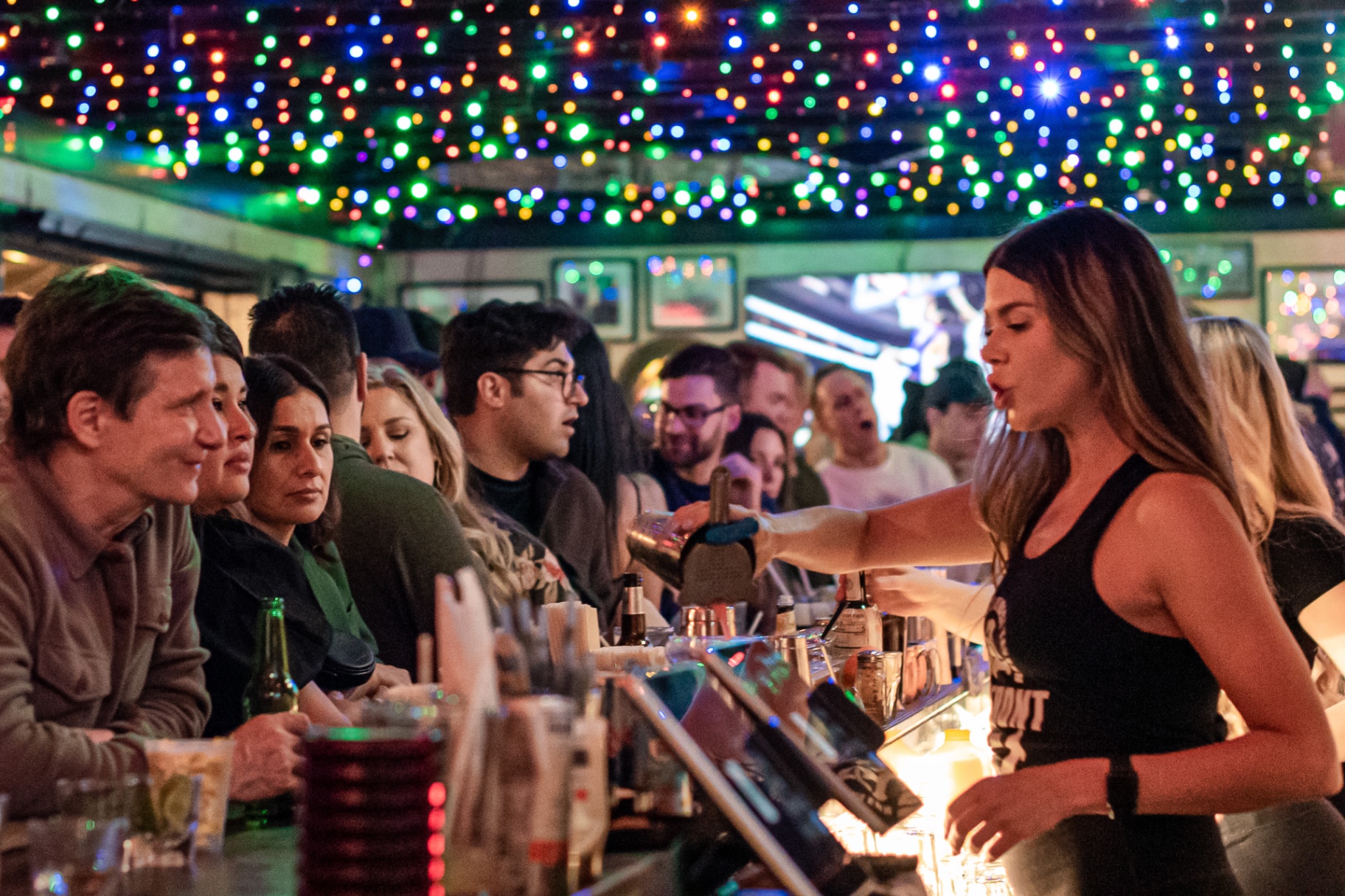 Waterfront Bar & Grill bartender pouring drinks under colorful string lights